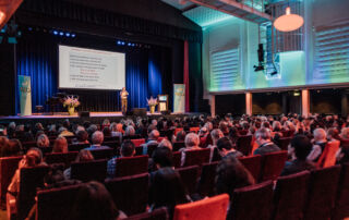 Congres bij Windesheim in Nieuwe Buitensociëteit Zwolle, met een spreker op het podium en een publiek van geïnteresseerde deelnemers.